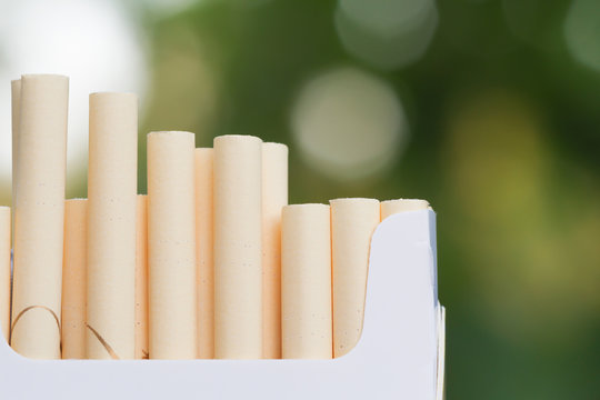 Open pack of cigarettes. Green blur background, closeup, selective focus