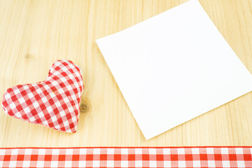 Ein rot weiß kariertes Herz mit weißem Zettel und kariertem Band am Bildunterrand, Holzhintergrund, Textfreiraum