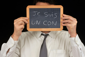 Homme cachant son visage avec une ardoise sur laquelle est écrit je suis un con