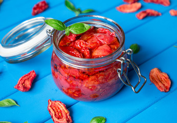Sun dried tomatoes with basil in a glass jar on a blue wooden table. Vegetarian concept