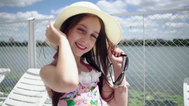 Happy teen girl in a hat on a pier near the lake in the summertime