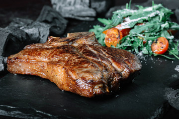 Grilled T-bone steak with tomatoes and spices on a cutting board on dark background