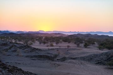 Colorful sunset over the Namib desert, Namibia, Africa. Mountains, dunes and Acacia trees silhouette in backlight. Orange red clear sky at the horizon.