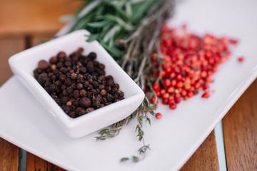 Rosemary with black and pink pepper corns on a white plate on wood background