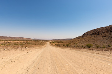Gravel 4x4 road crossing the colorful desert at Twyfelfontein, in the majestic Damaraland Brandberg, scenic travel destination in Namibia, Africa.