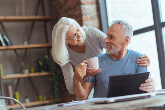Positive aged wife giving a cup of tea to her husband