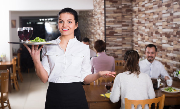 young woman waiter bringing order for  guests