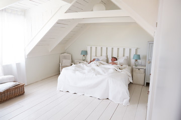 Fototapeta na wymiar Couple Sleeping In Light And Airy White Bedroom