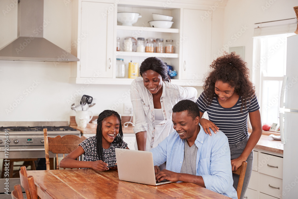 Poster family around kitchen table booking vacation on laptop together