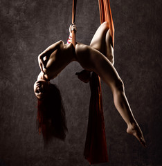 Beautiful nude dancer on aerial silk, graceful contortion, acrobat performs a trick on a ribbons