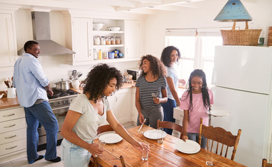 Family With Teenage Daughters Laying Table For Meal In Kitchen