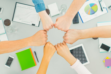 The six people hold fists at the table. view from above