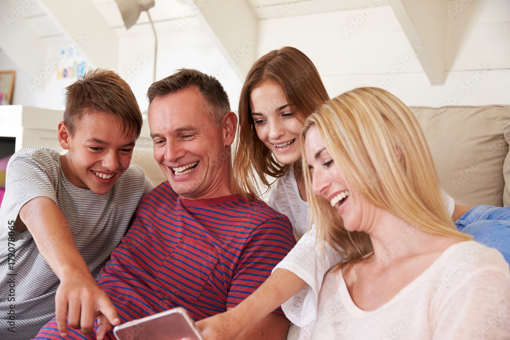 Wall mural family with teenage children sitting on sofa looking at mobile phone at home