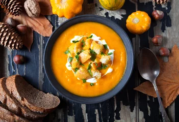 Foto op Plexiglas Gerechten Pumpkin and carrot soup with cream and crackers, croutons autumn food dish for Thanksgiving, halloween on dark old wooden background. Top view. close up. Flat lay autumn vegetables.