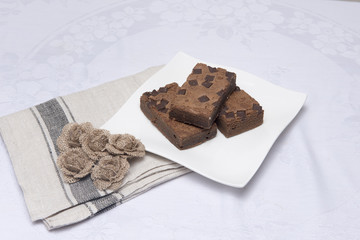 Chocolate brownie slices on a white plate with hessian flowers