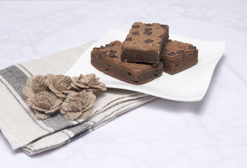 Chocolate brownie slices on a white plate with hessian flowers 