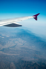 Aerial view from airplane looking outside window. Airplane wing with background of blue sky and green forest land. Concept of travel, holiday, vacation.