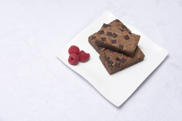Chocolate brownie slices with raspberries on a white plate 