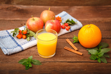 Refreshing orange juice in a glass on a wooden background. Berry berries, apples, mint, melissa...