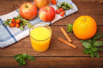 Refreshing orange juice in a glass on a wooden background. Berry berries, apples, mint, melissa...