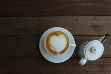 A cup of coffee with heart pattern in a white cup on wooden background