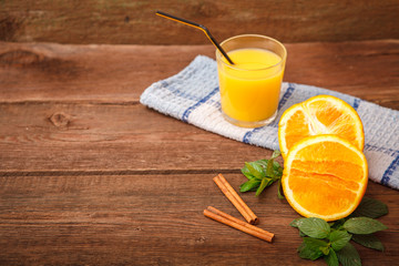 Refreshing orange juice in a glass on a wooden background. Mint, lemon balm leaves, orange and cinnamon with fruit juice on the table. Vitamins. Space for text.
