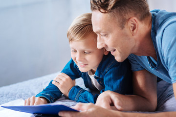 Little son and father reading together on bed