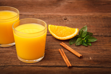 Orange juice in a glass on a wooden background with orange and melissa and cinnamon. Space for text.