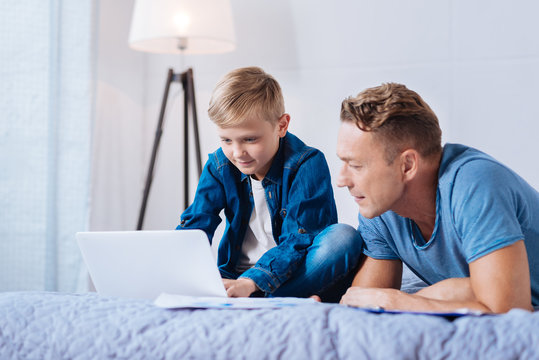Pleasant father watching his son working on laptop