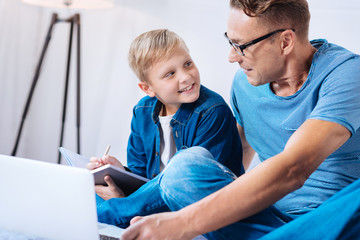 Obraz premium Little boy exchanging smiles with father while making notes