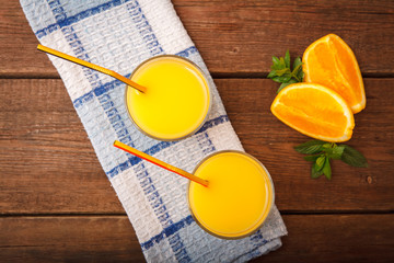 Orange juice in a glass on a wooden background with orange and melissa.