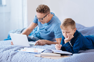 Little boy studying while his father working on laptop