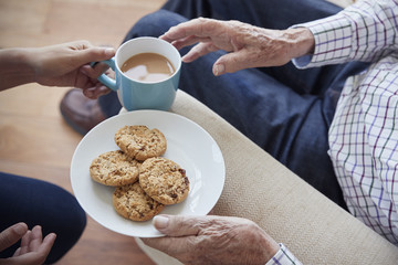 Woman passes tea and biscuits to a seated senior man, detail