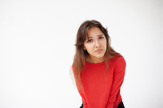 Picture of brunette Hispanic female in red sweater leaning forward, frowning. Irritated woman making grimace and staring at camera, having indignant, displeased or annoyed facial expression