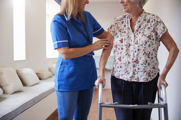 Nurse helping senior woman use a walking frame, mid section - Powered by Adobe