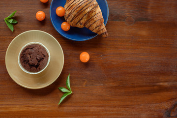 Morning breakfast: blue cup of tea, chocolate croissant, muffins and physalis on a wooden table. Flat composition