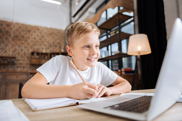 Cheerful boy copying information from laptop to notebook