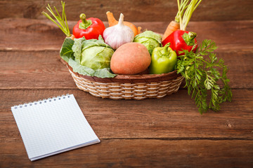 Fresh vegetables in a basket on a wooden background. Cabbage, bell pepper, potatoes, garlic, onion, chili and carrots. Harvest. Thanksgiving Day. Space for text.