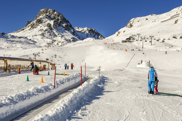 Winter resort with children's ski school area with magic carpet conveyor,instructor ans ski slopes between mountains on the background