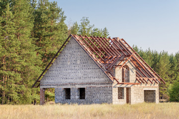 Fototapeta na wymiar Unfinished house of foamed concrete with metal roof construction at countryside near forest