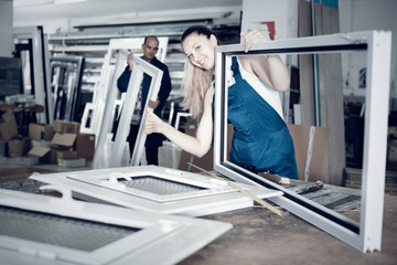 workwoman with plastic window frame in workshop giving thumbs up