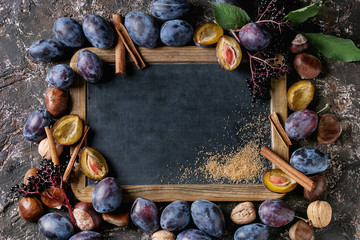 Autumn frame from plums, nuts, cinnamon and brown sugar with empty vintage chalkboard over brown...