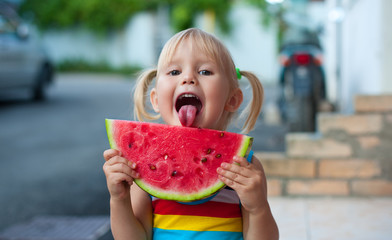 Happy three-year-old little European girl blonde with tails eating a watermelon