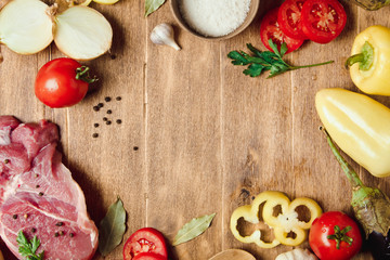 Raw meat on a wooden chopping board with fresh organic vegetables, onion, garlic, spices, peppercorn, salt, tomatoes and parsley for cooking. Kitchen ideas. Lunch, dinner