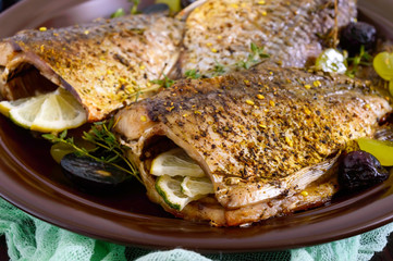 Baked carp with grapes and herbs on a ceramic dish on a dark wooden background.