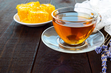 A cup of tea and honeycomb on a dark wooden table.