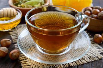 A cup of fresh fragrant herbal tea with honey and hazelnuts on a dark wooden background. Close-up.