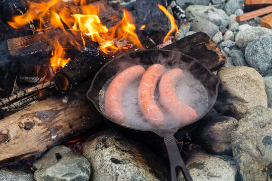Cooking sausages in cast iron skillet on campfire while camping. Good and positive campfire food.