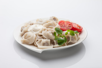 Pelmeni with tomatoes and oregano. On white plate and white background.