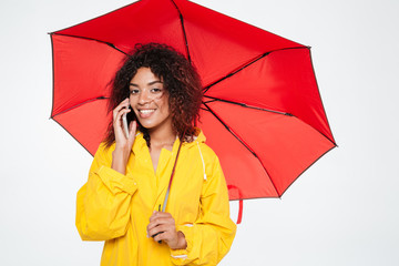 Smiling beautiful african woman in raincoat hiding under umbrella